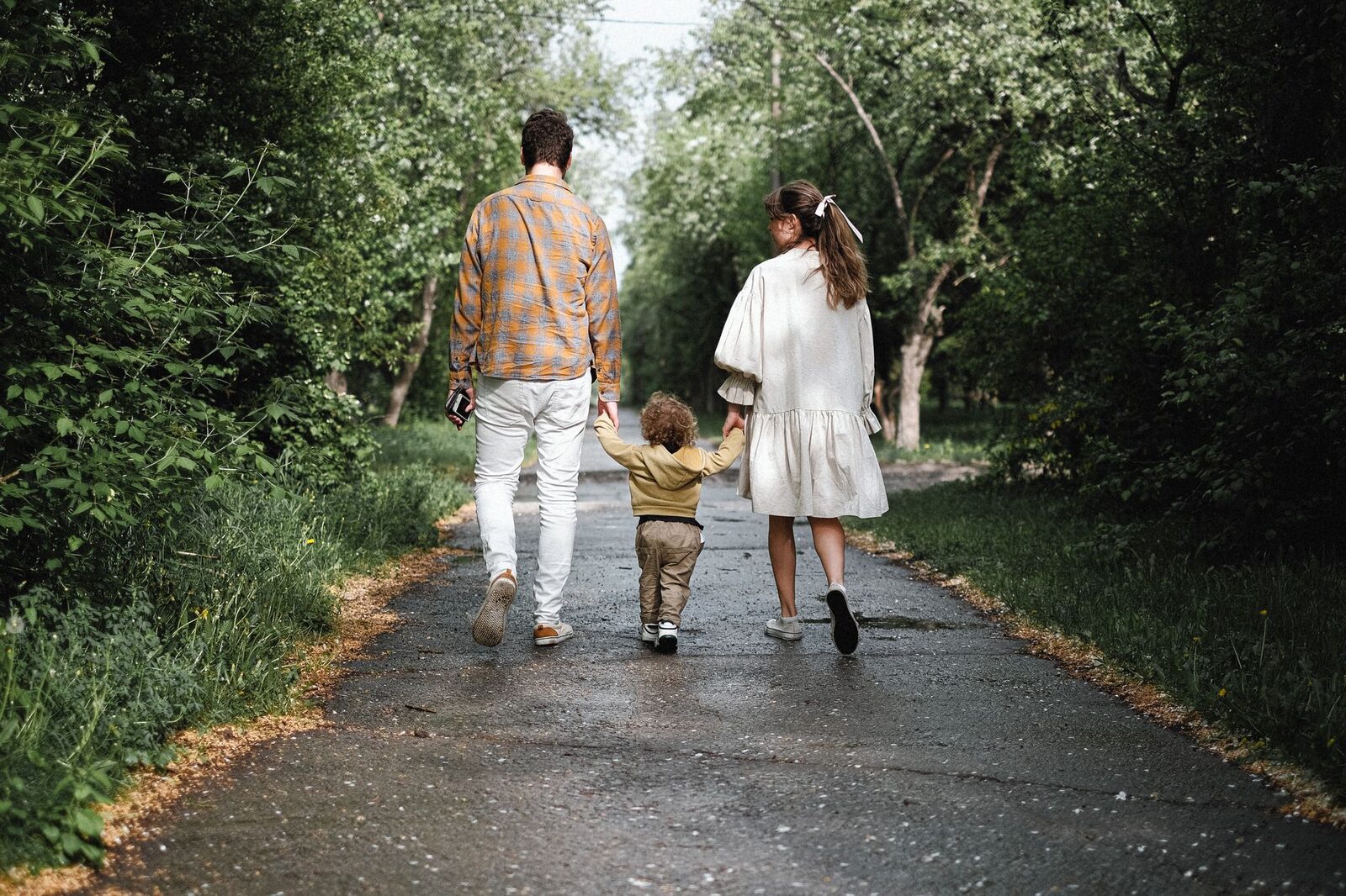 A couple and toddler enjoy a peaceful walk on a tree-lined path in a lush park.