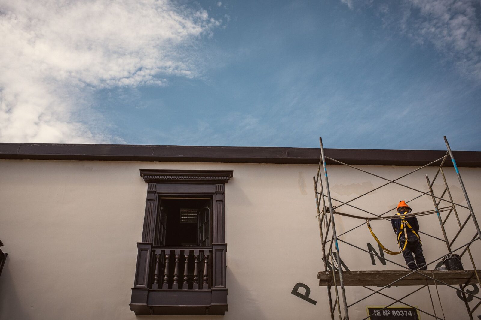 A construction worker wearing safety gear stands on scaffolding beside a traditional building.